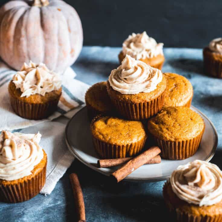Freshly baked pumpkin spice cupcakes sitting on a table. Some frosted with cream cheese frosting.