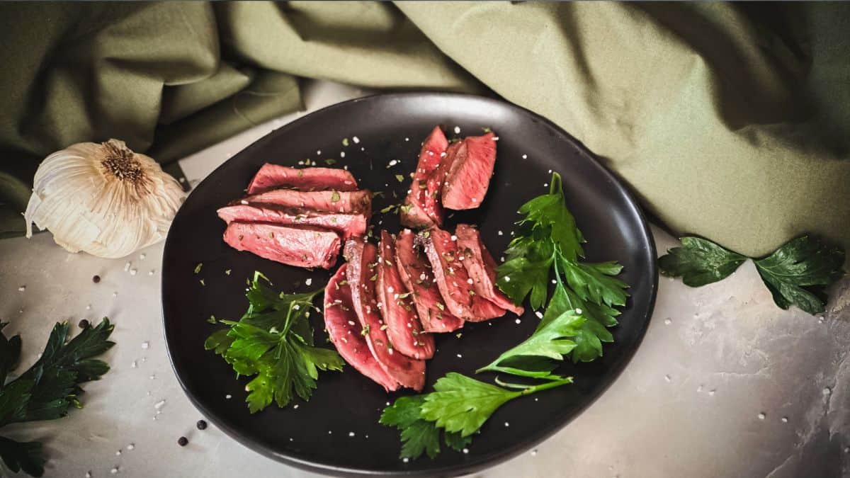 Pan-fried deer heart slices garnished with fresh parsley on a black plate, showcasing a rustic and adventurous dish.