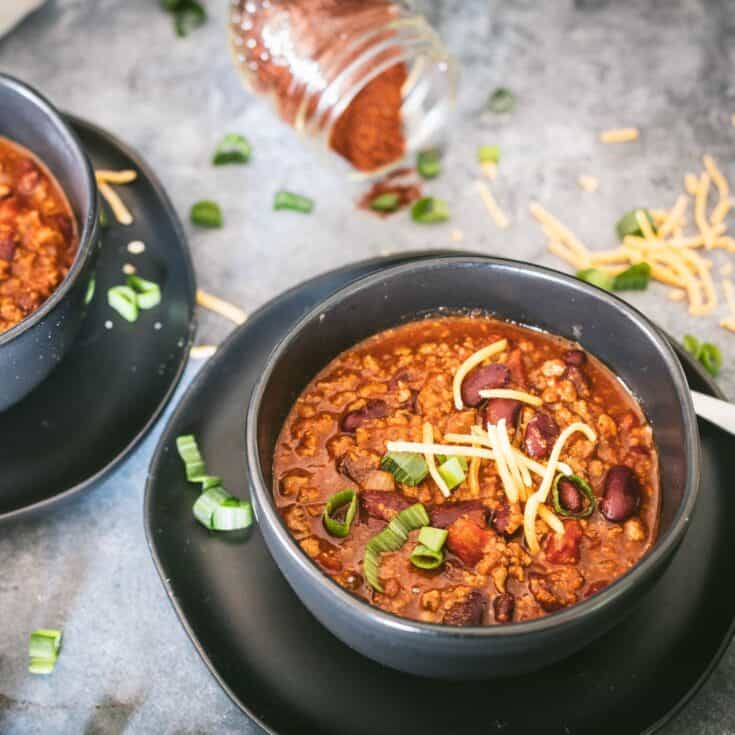 Bowl of venison chili topped with shredded cheese and green onions.