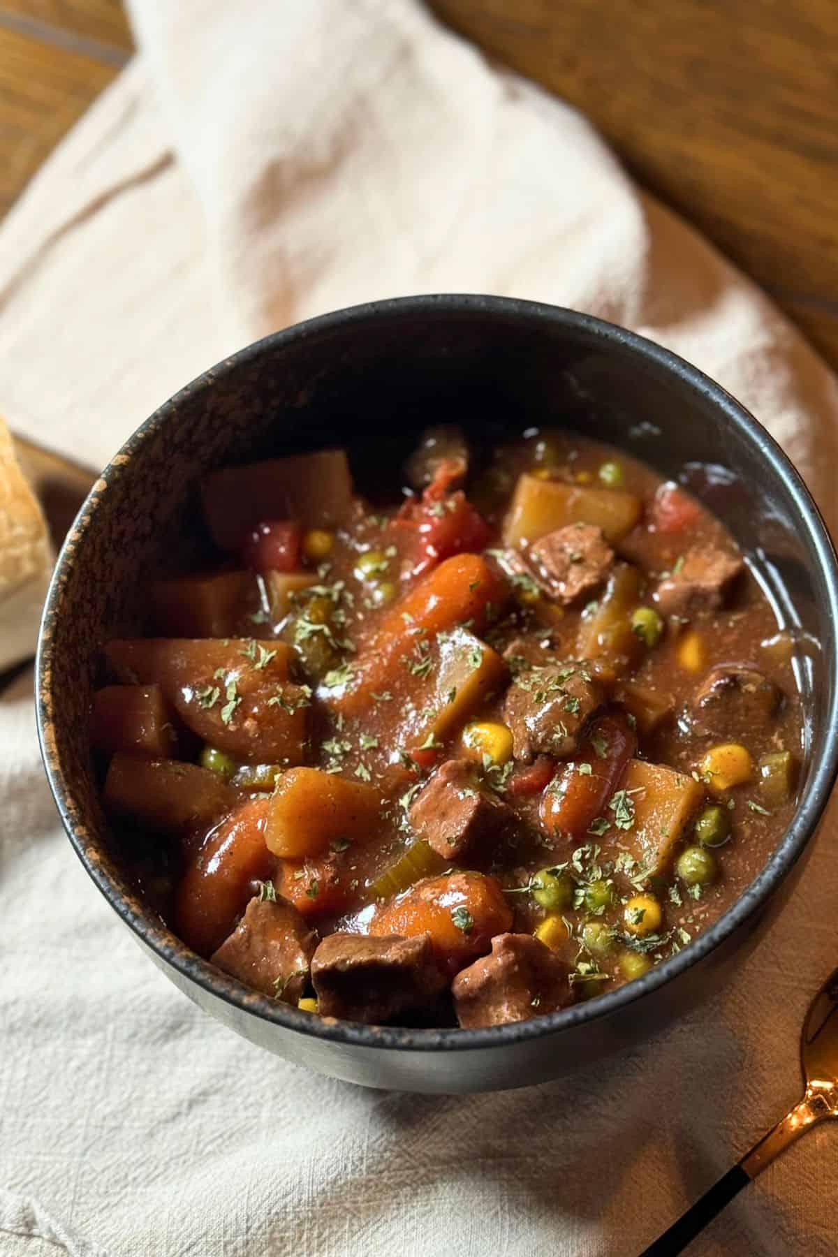 Bowl of old-fashioned vegetable beef stew with tender beef, potatoes, carrots, peas, and corn in a thick savory broth, served with bread.