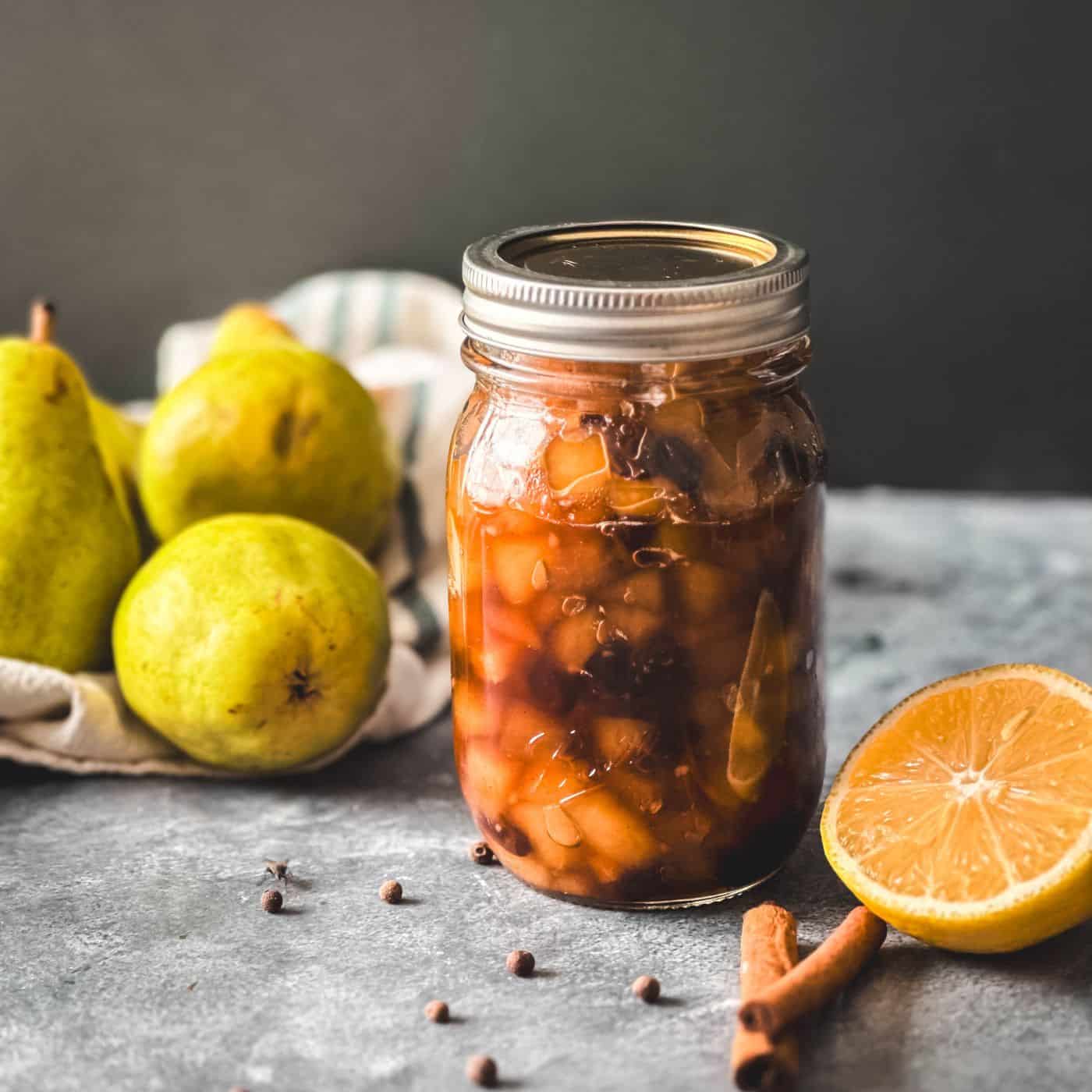 Jar of spiced pear chutney with fresh pears and fresh sliced lemon in the background.