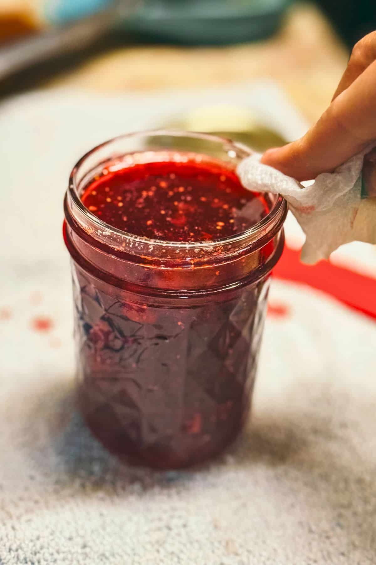 Elle wiping the rim of a jar filled with homemade Christmas jam before sealing and processing during the canning stage.