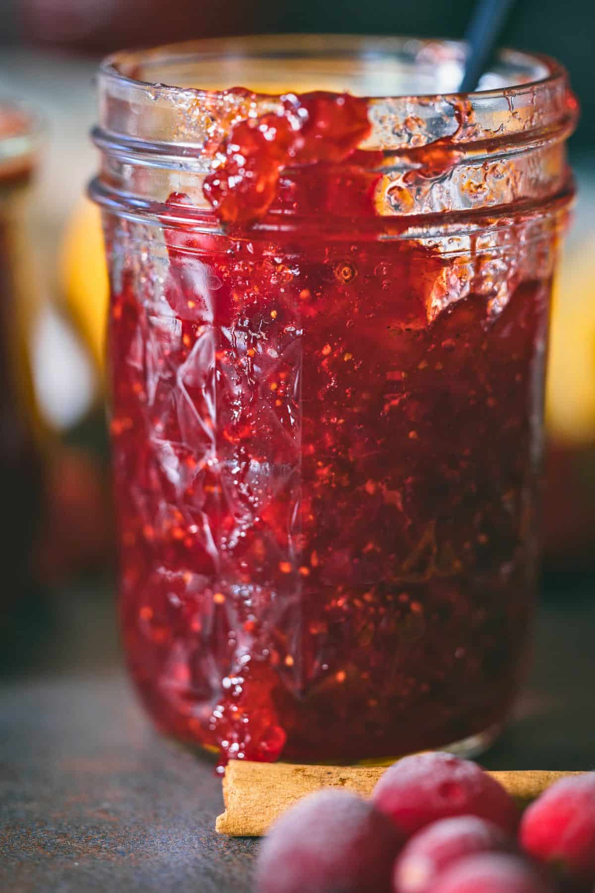 Jars of homemade Christmas jam made with cranberries, strawberries, and oranges, showing the rich red color and perfect set.