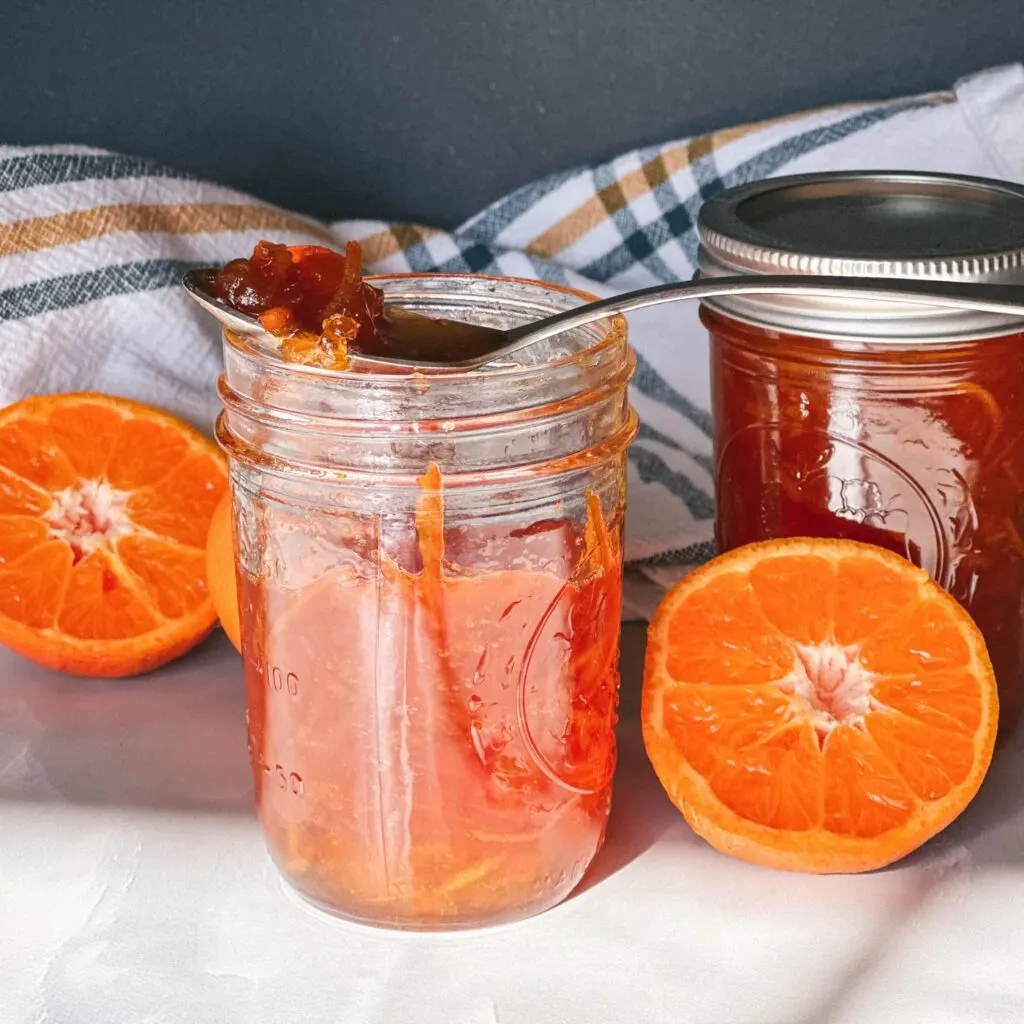Jars or orange marmalade on a counter with fresh oranges