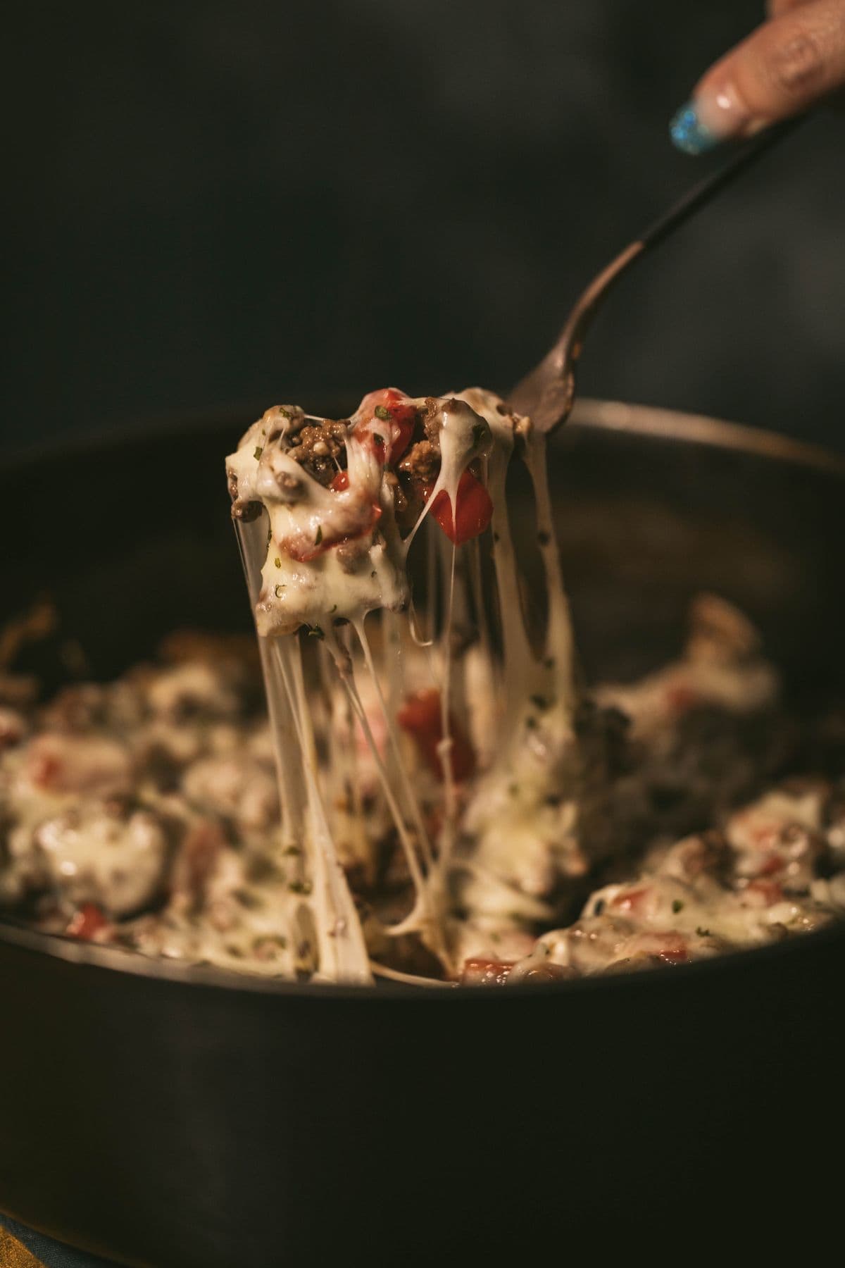 Ground venison skillet with melted cheese and peppers being lifted by a fork, showcasing a comforting, hearty dish.