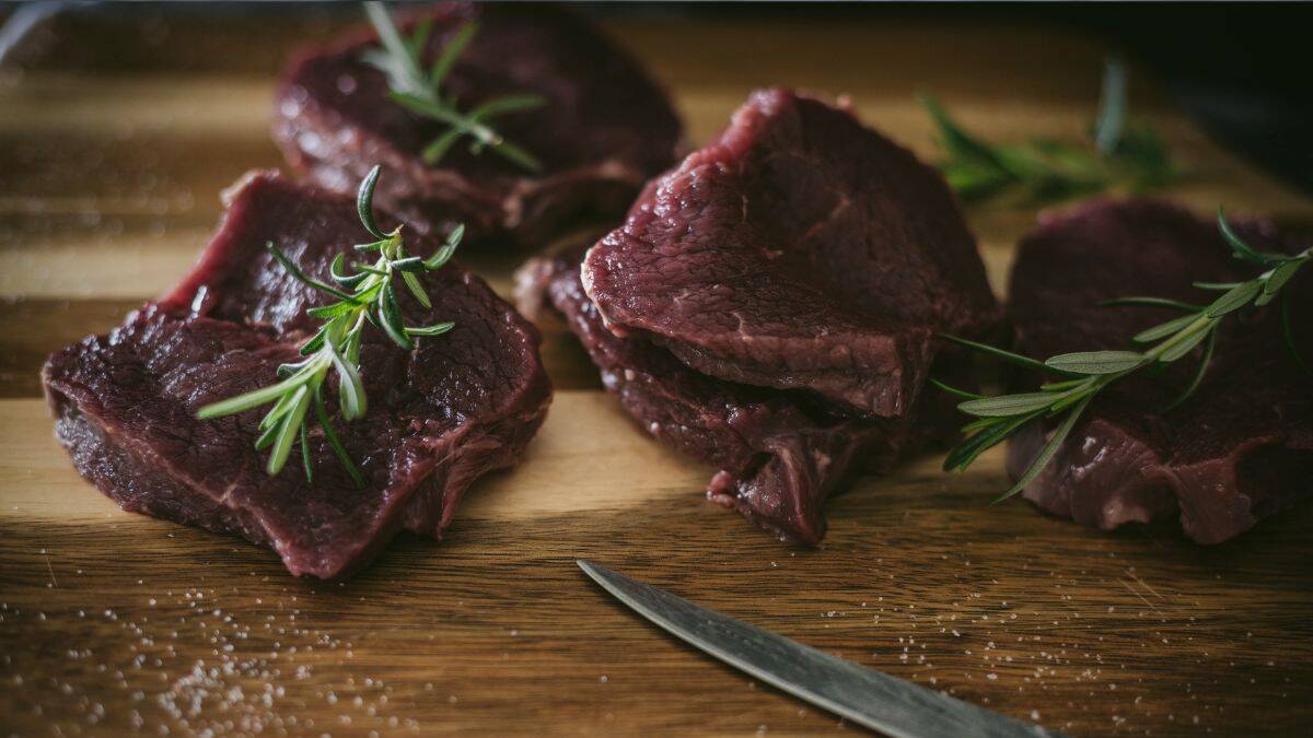 Raw venison backstrap medallions with rosemary on a wooden cutting board, showing lean texture and deep red color.