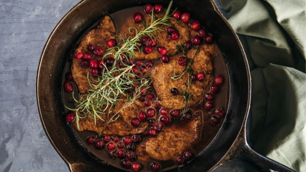 Cast iron skillet filled with seared pork chops simmered in a cranberry and red wine sauce, topped with fresh rosemary and thyme.