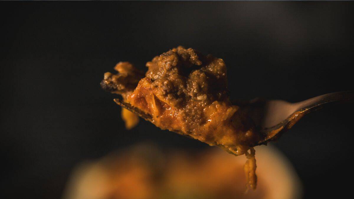 Close-up of a forkful of cheesy ground venison enchilada with rich sauce