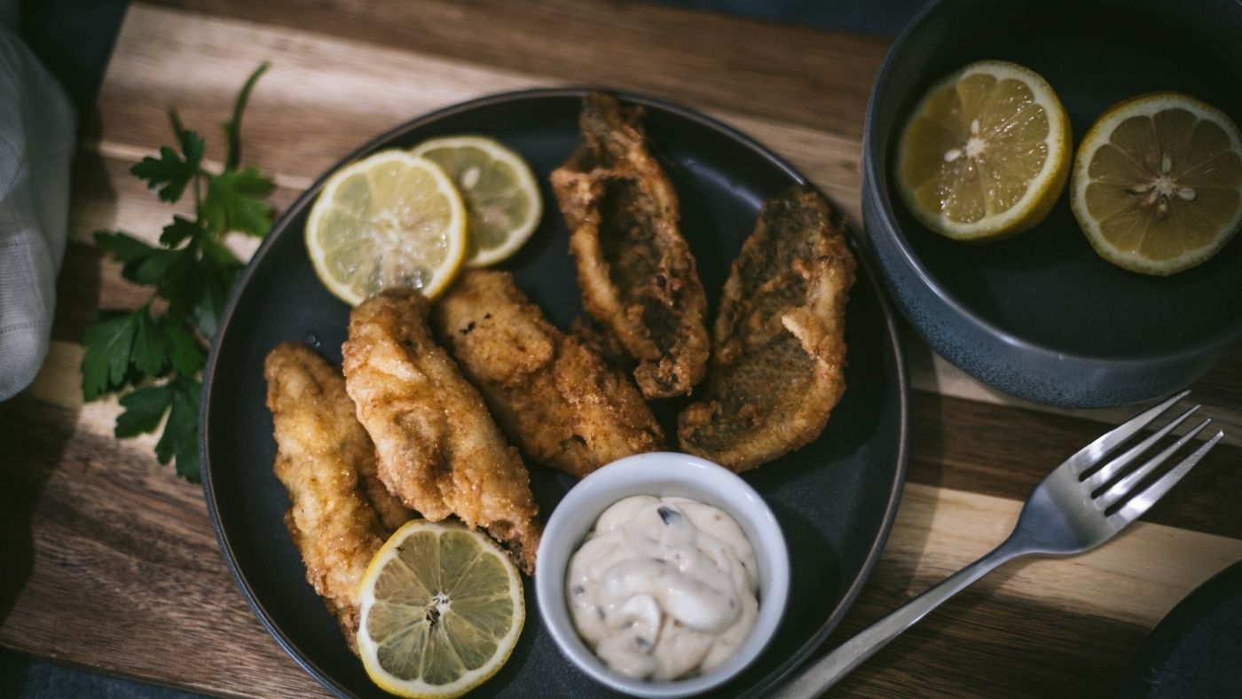 Pan fried bluegill fillets on a plate with tartar sauce and lemon