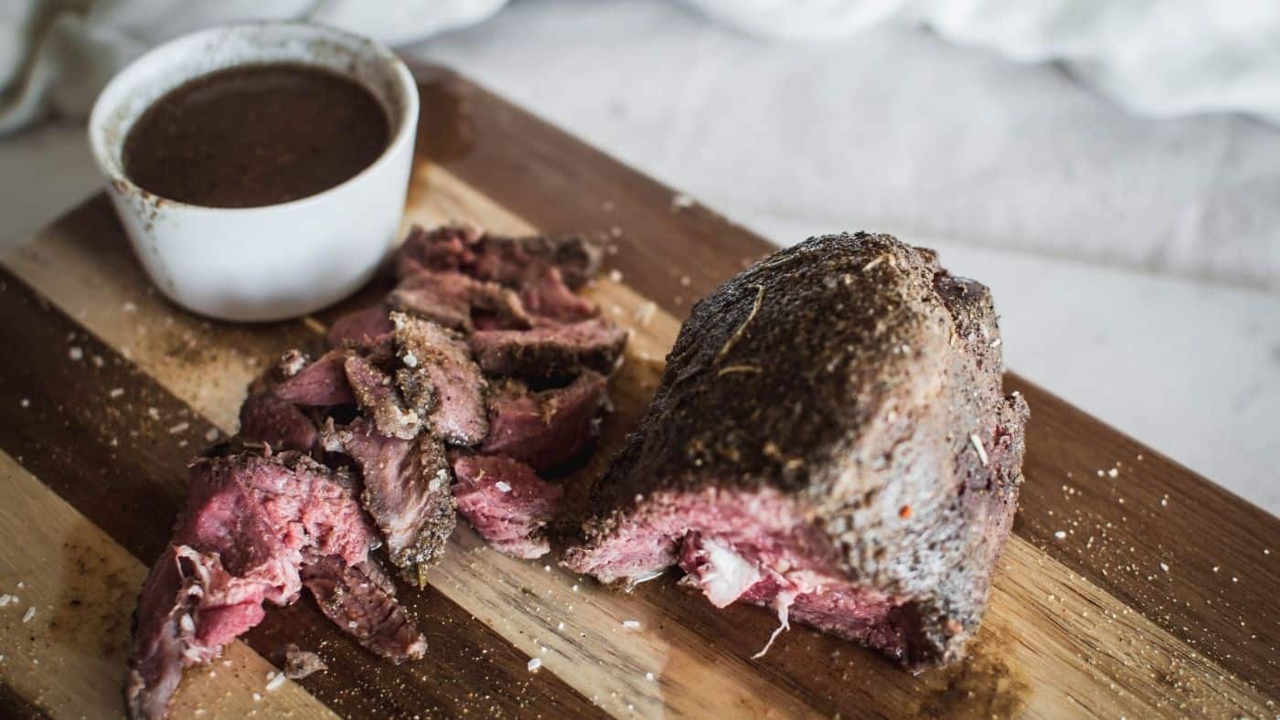 Sous vide venison roast sliced on a cutting board with au jus.