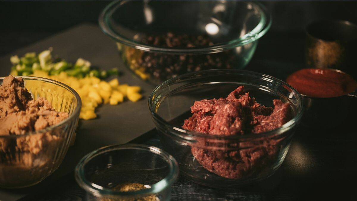 Ingredients for venison enchiladas including ground venison, refried beans, black beans, chopped peppers, and enchilada sauce in glass bowls.