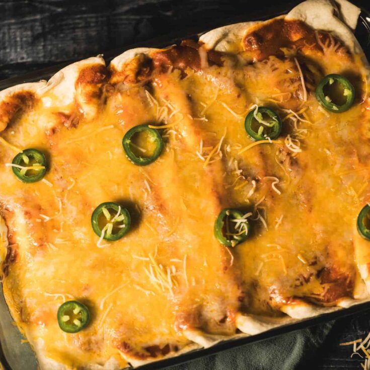 Baked venison enchiladas topped with melted cheese and sliced jalapeños in a glass pan.