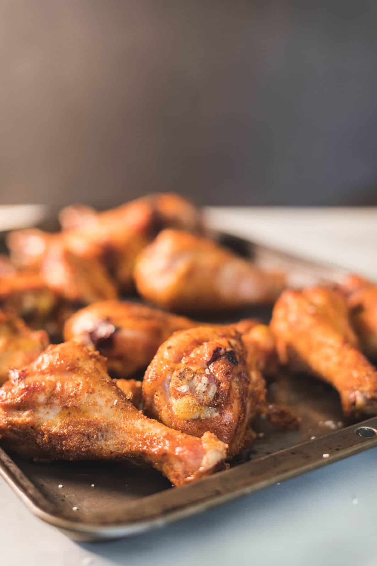 Close-up of crispy smoked chicken legs on a baking sheet, showing golden skin and savory dry rub texture.