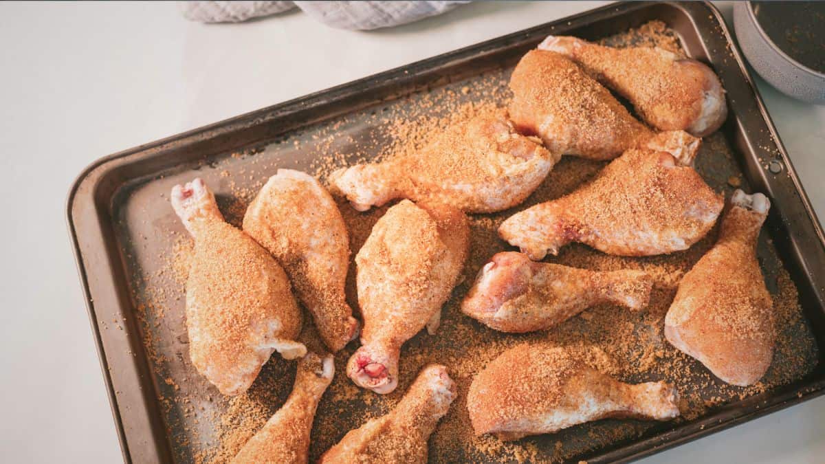 Raw chicken drumsticks coated in dry rub, resting on a baking sheet before going on the smoker.