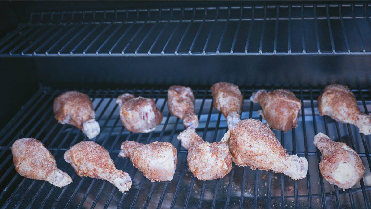 Chicken drumsticks coated in dry rub arranged on a Traeger smoker at the start of the smoking process.