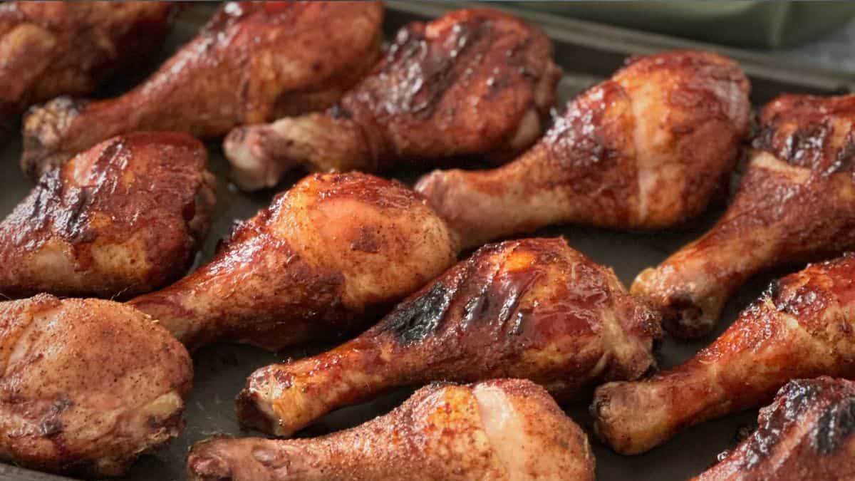 Tray of smoked chicken legs with crispy skin, seasoned with dry rub and grilled to golden brown on a pellet smoker.