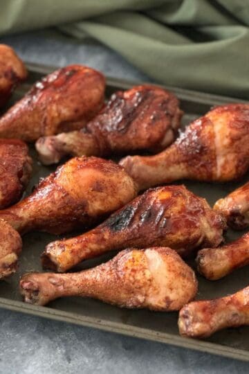 Tray of smoked chicken legs with crispy skin, seasoned with dry rub and grilled to golden brown on a pellet smoker.