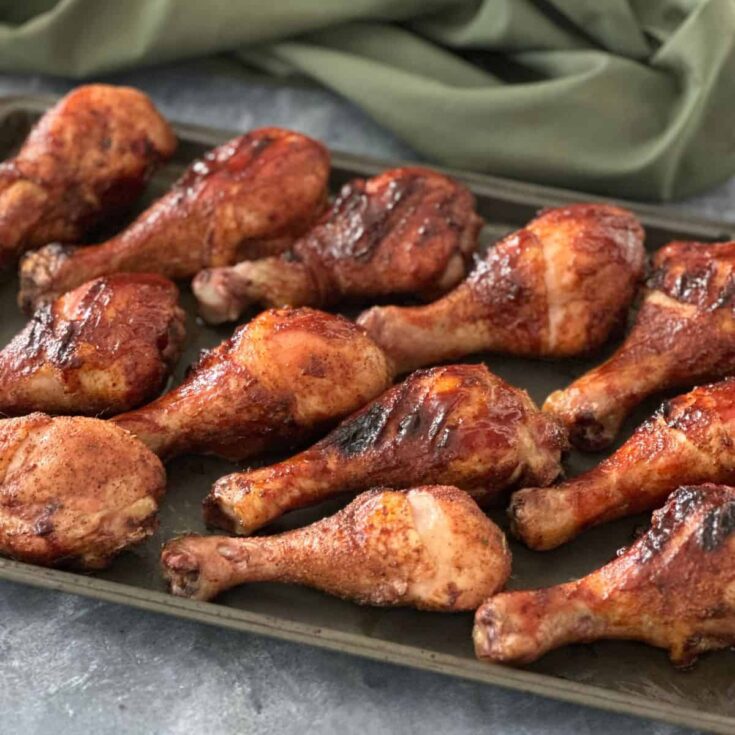 Tray of smoked chicken legs with crispy skin, seasoned with dry rub and grilled to golden brown on a pellet smoker.