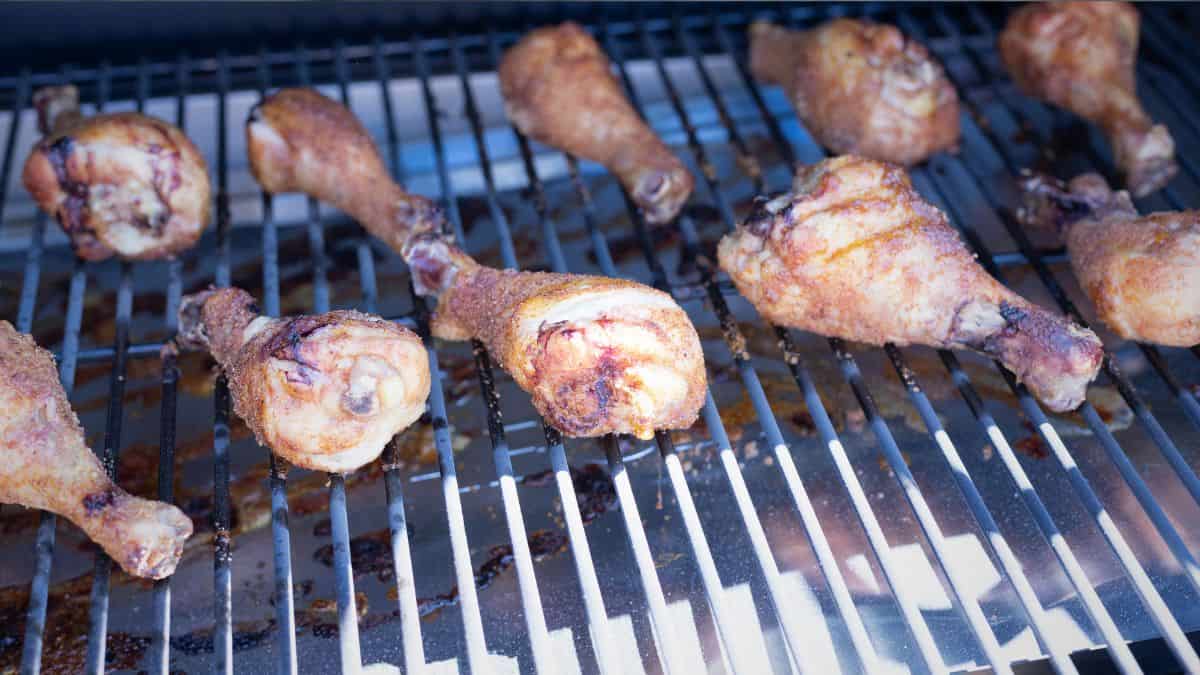 Seasoned chicken drumsticks smoking on a pellet grill at 225°F, beginning to crisp on the grates.