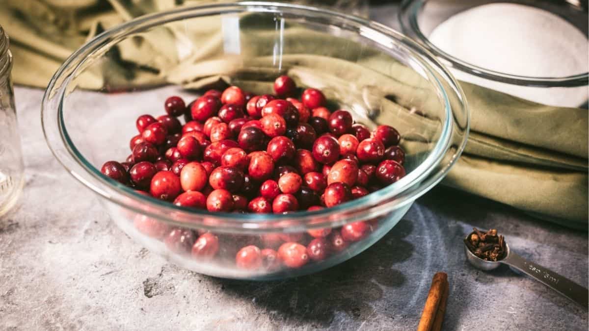 Fresh cranberries in a glass bowl with sugar, cloves, and cinnamon ready to make homemade canned cranberry sauce