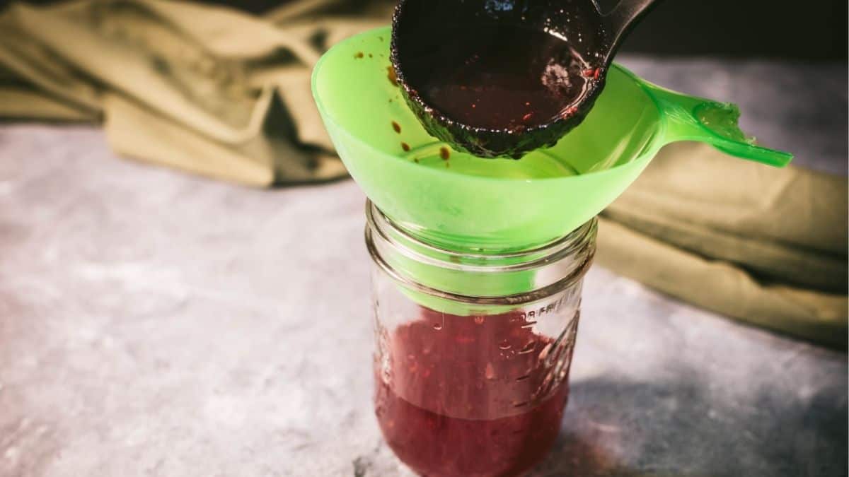 Ladling hot cranberry sauce through a canning funnel into a glass jar before processing in a water bath canner.