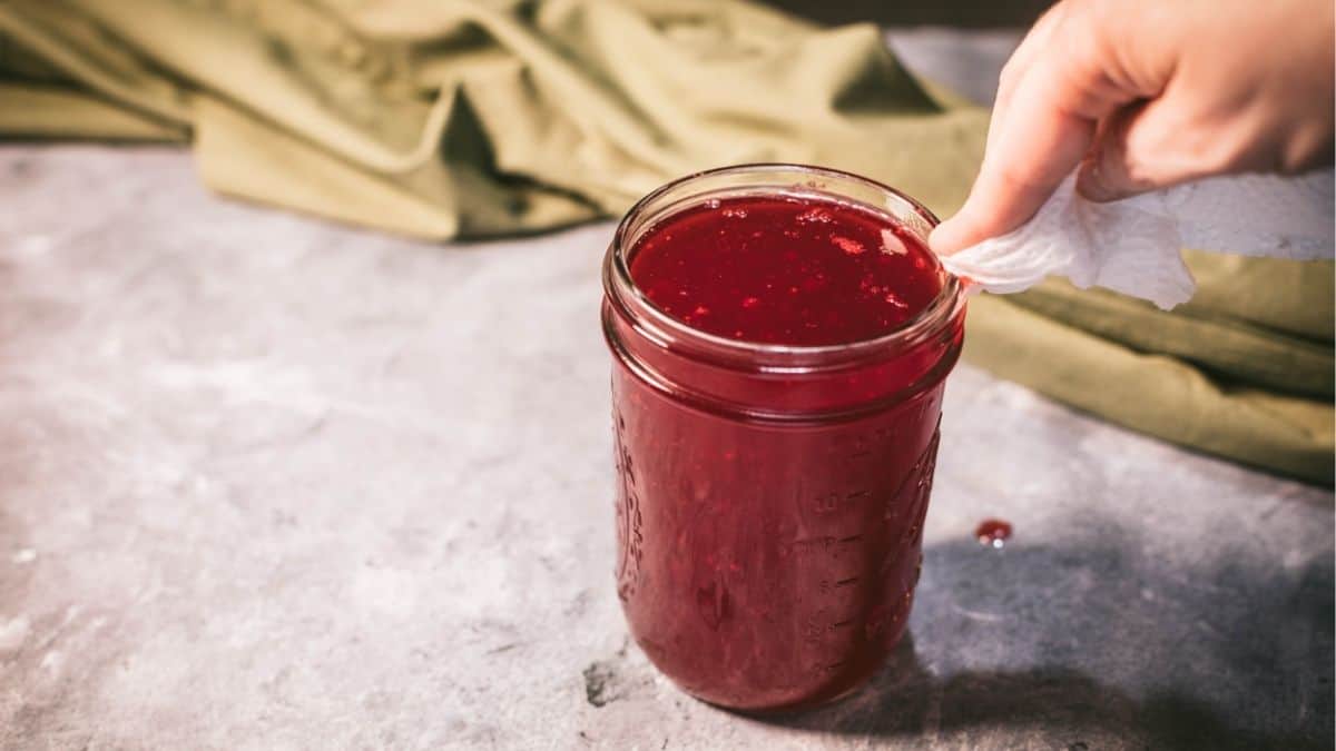 Wiping the rim of a jar filled with homemade jellied cranberry sauce before canning.