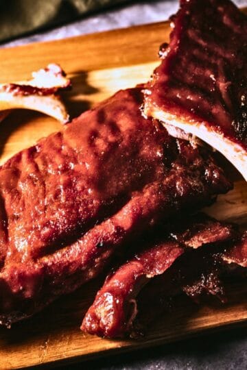 Close-up of saucy smoked pork ribs on a wooden cutting board, cooked using the 3-2-1 method until tender and falling off the bone.