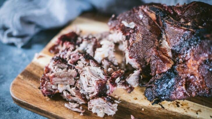 Smoked pork butt on a board and pulled apart into pulled pork.