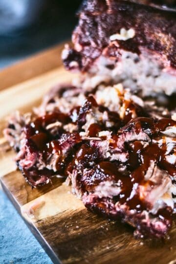 Close-up of juicy smoked pork butt shredded into pulled pork and topped with barbecue sauce on a wooden cutting board