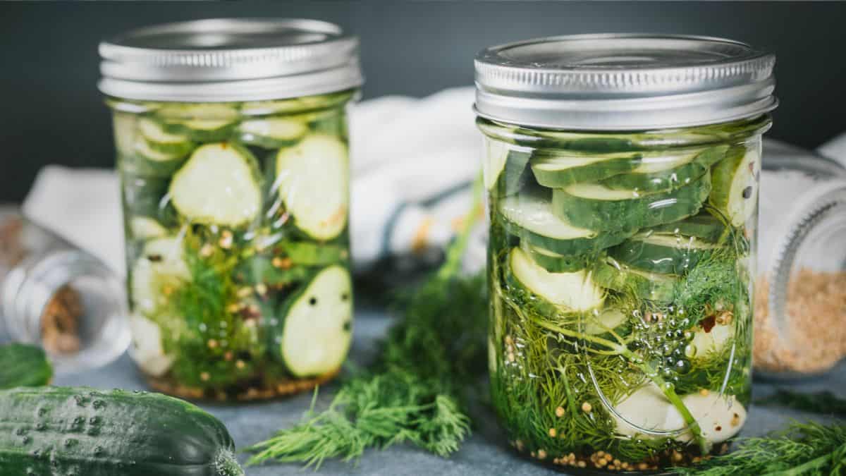 Crunchy homemade dill pickles in mason jars with garlic, dill, and pickling spices on a kitchen counter.