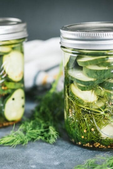 Crunchy homemade dill pickles in mason jars with garlic, dill, and pickling spices on a kitchen counter.
