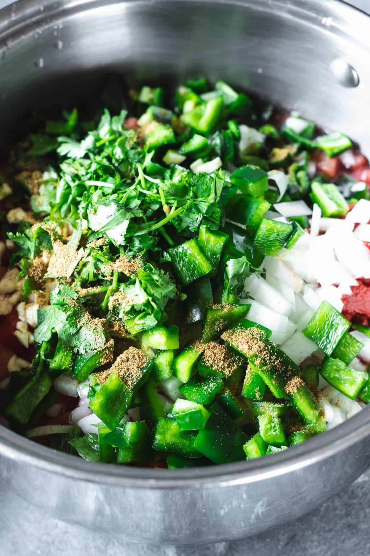 Chopped green peppers, onions, cilantro, garlic, and spices in a stainless steel pot for homemade salsa