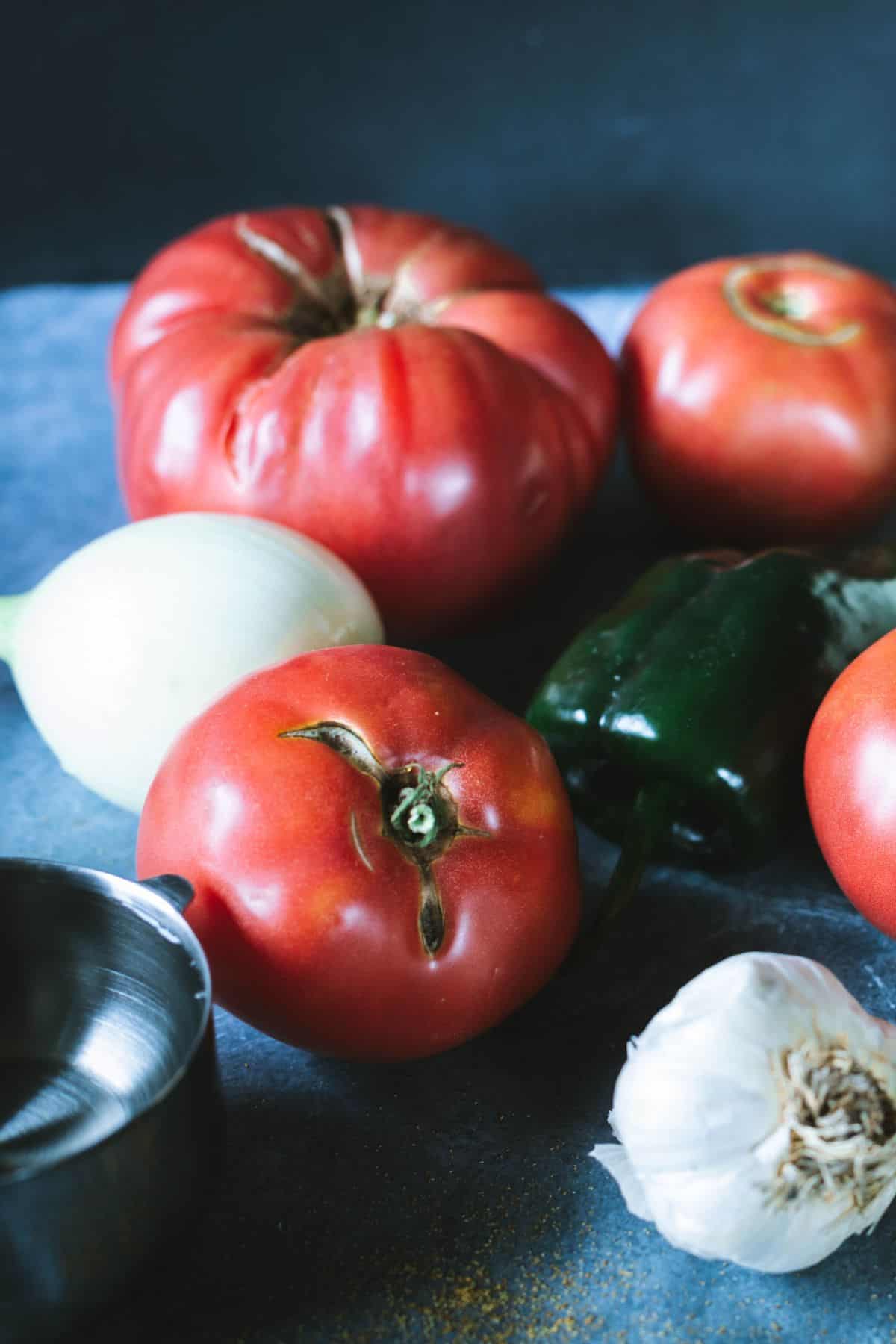 Fresh tomatoes, white onion, garlic, and green pepper on a dark countertop for homemade salsa
