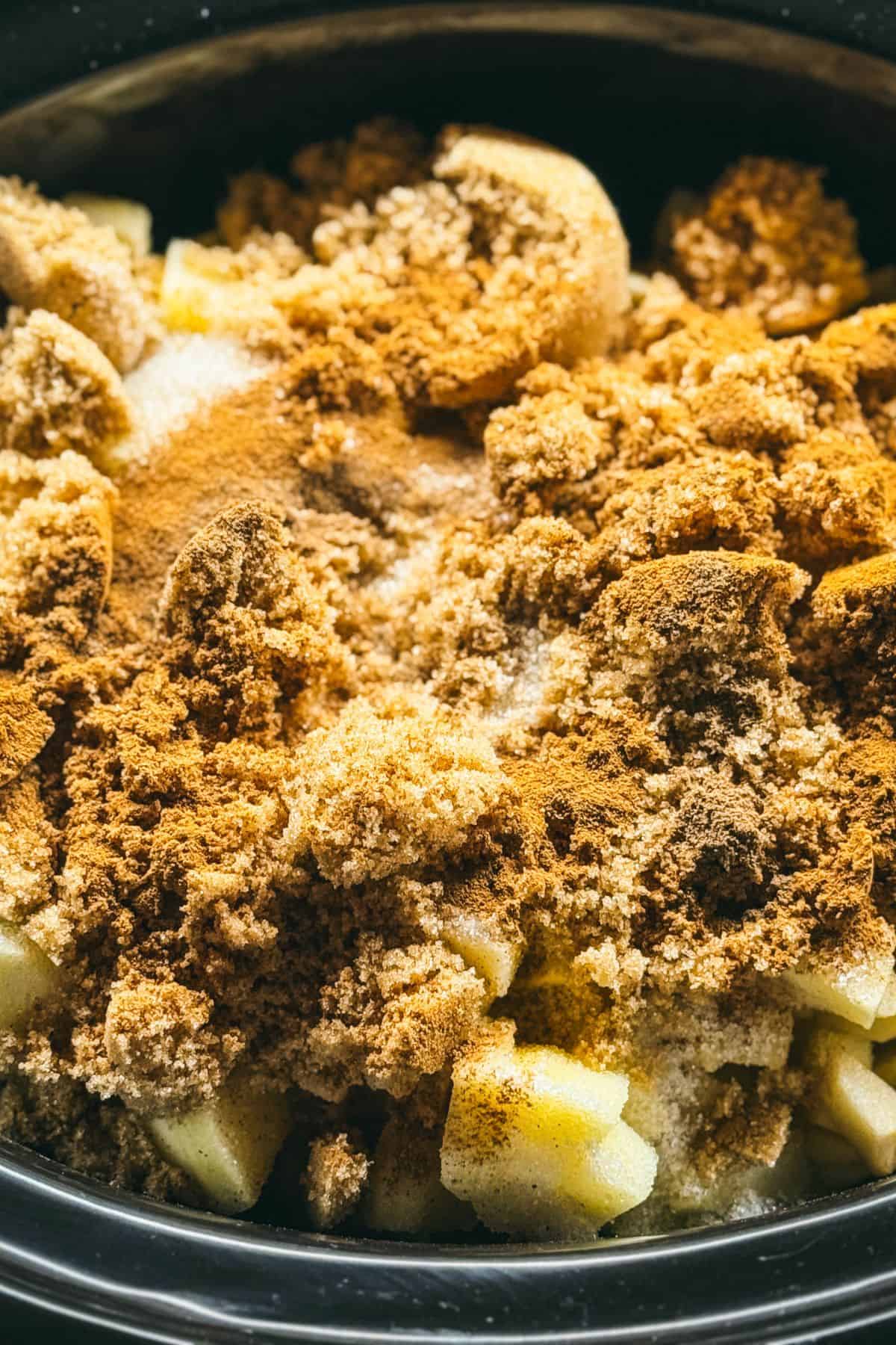 Close-up of apples, brown sugar, and warm spices in a slow cooker, the ingredients needed to make homemade apple butter.