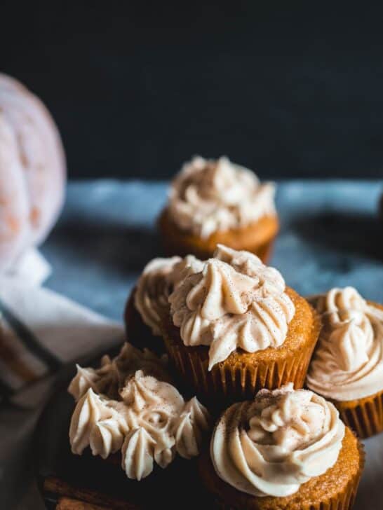 Pumpkin spice cupcakes topped with cream cheese frosting sitting on a plate and counter.