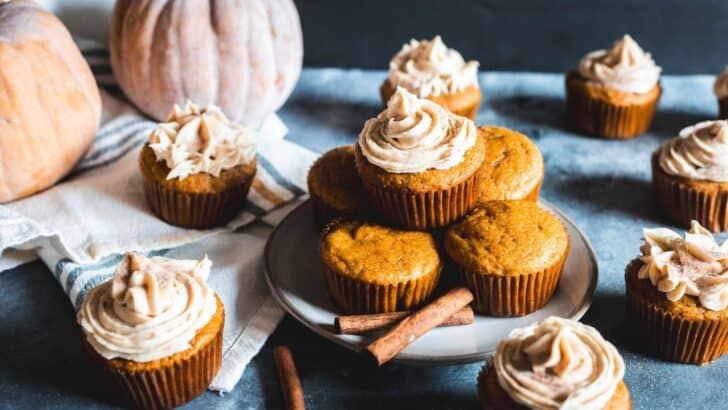 Freshly baked pumpkin spice cupcakes sitting on a table. Some frosted with cream cheese frosting.