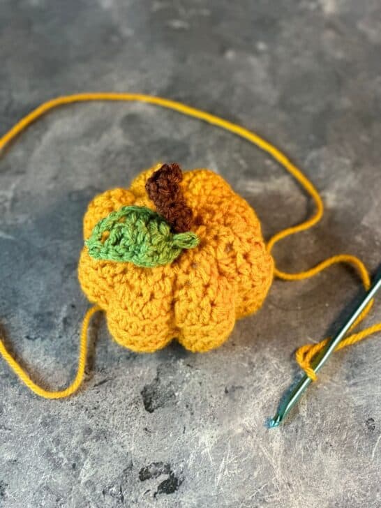 Overhead shot of orange crochet pumpkin with brown crocheted stem and green crocheted leaf