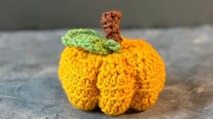 Closeup of orange crochet pumpkin with brown stem and green leaf.