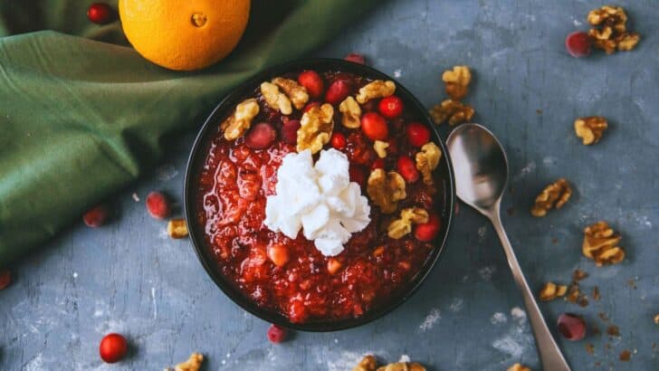 A bowl of cranberry jello salad on a counter topped with whipped cream and walnuts.