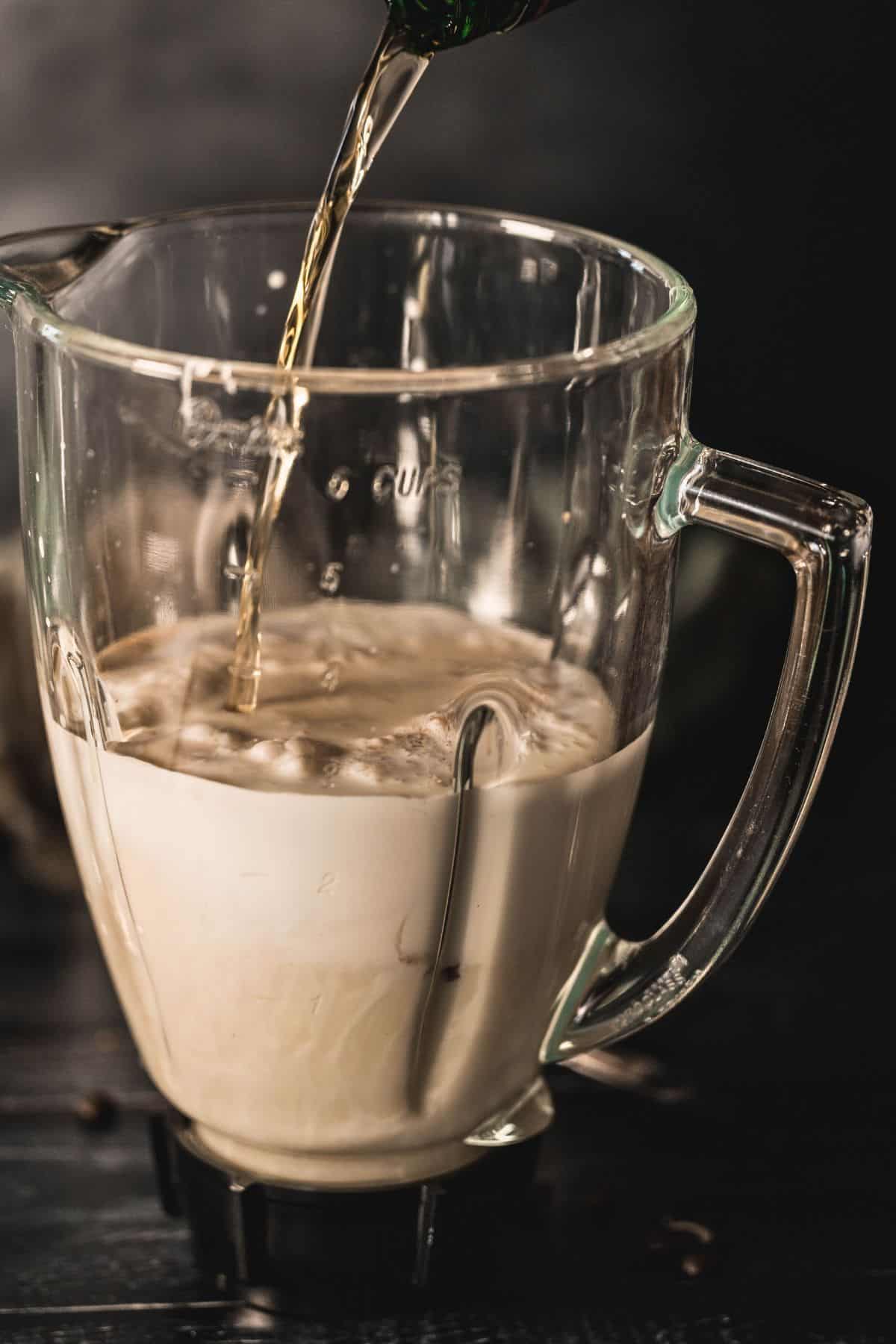 Irish whiskey being poured into a blender filled with cream and condensed milk for homemade Irish cream liqueur.