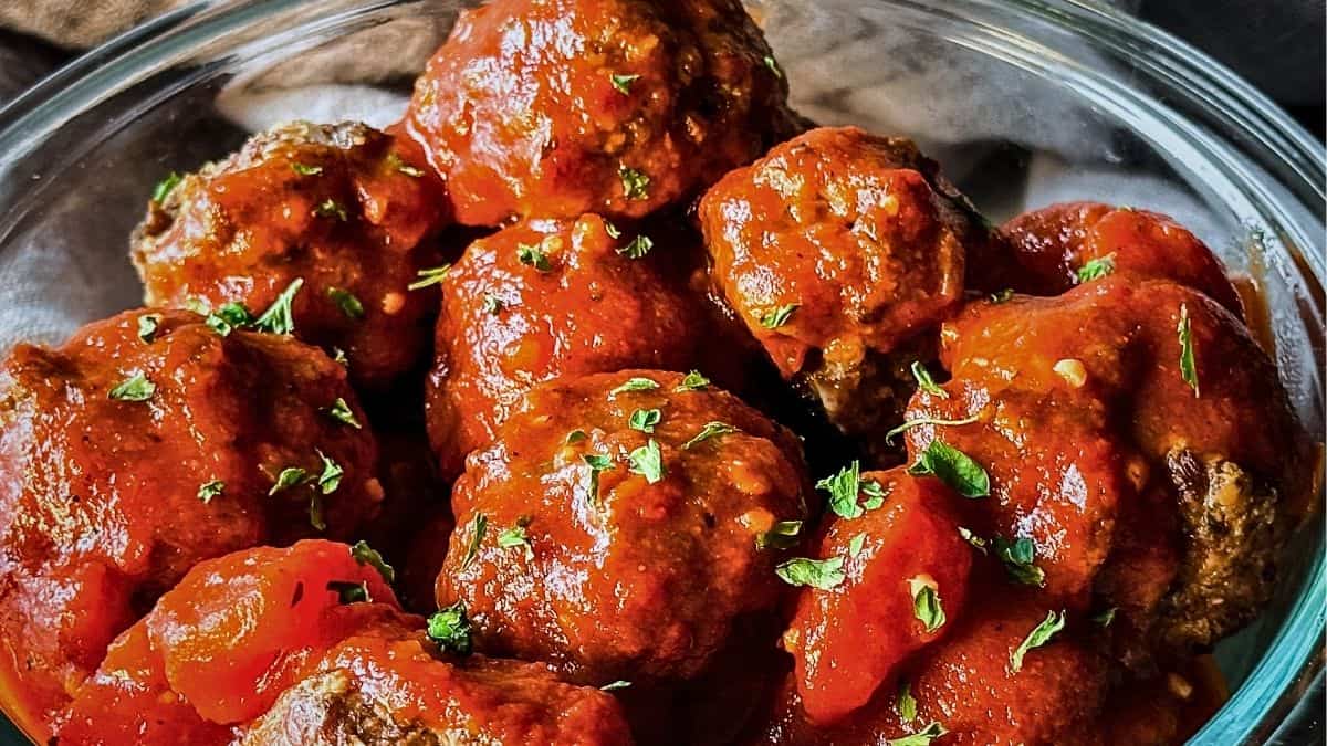 close-up of baked venison meatballs coated in rich tomato sauce and sprinkled with fresh parsley in a glass bowl