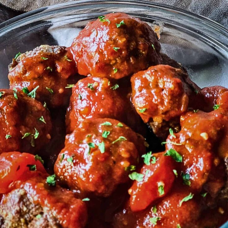 close-up of baked venison meatballs coated in rich tomato sauce and sprinkled with fresh parsley in a glass bowl