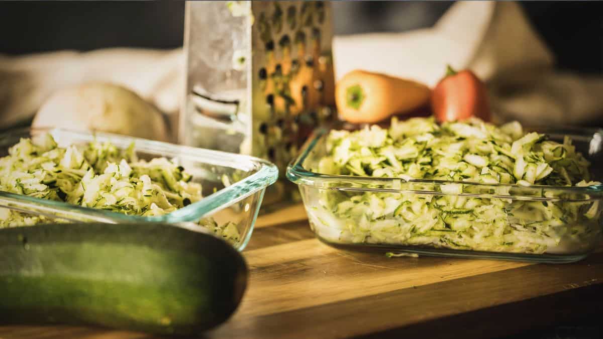 Coarsely grated zucchini in glass containers with a box grater and fresh vegetables