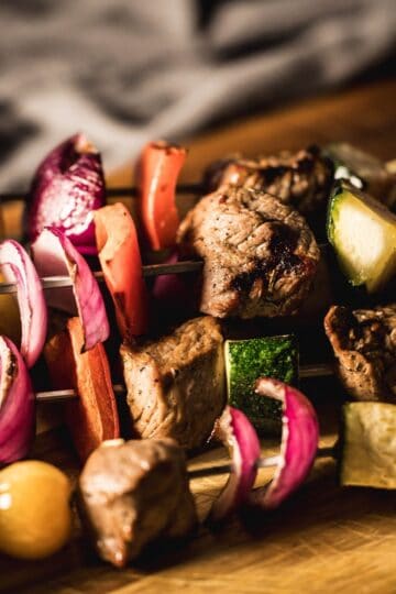 Grilled venison kabobs with zucchini, red onion, bell pepper, and summer vegetables on metal skewers.