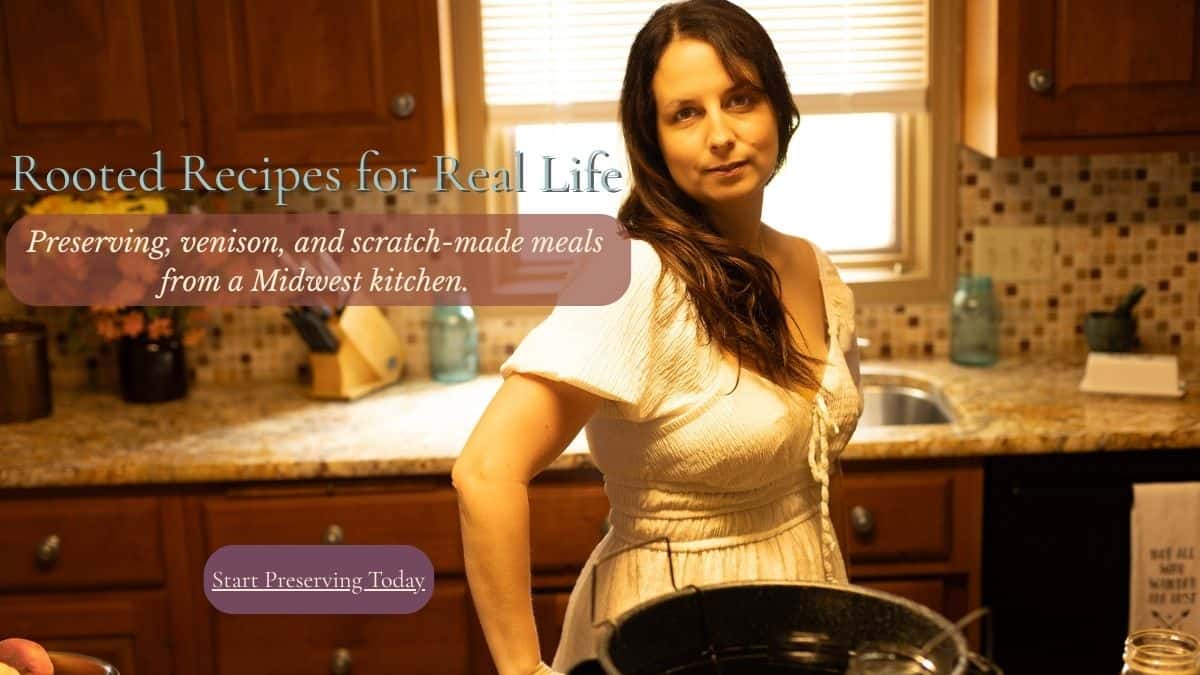 Elle McCoy standing in a warm, Midwest kitchen with a canning pot on the counter, promoting seasonal preserving, venison, and scratch-made meals on The Rustic Elk homepage.