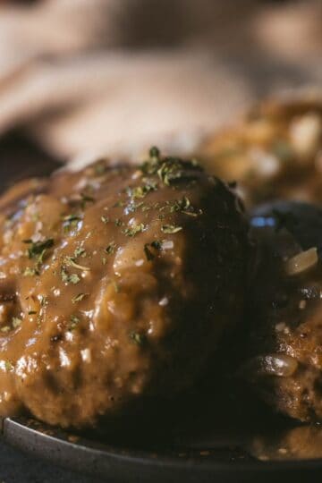 Close-up of tender venison Salisbury steak smothered in rich onion gravy and garnished with parsley.