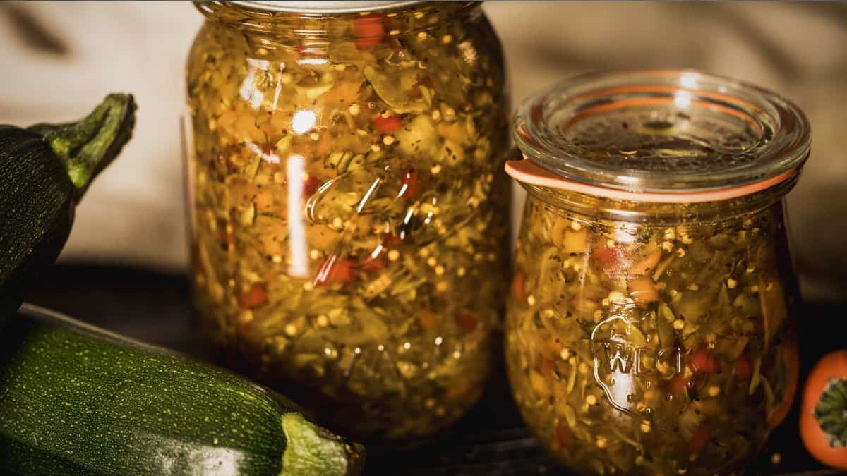 Homemade zucchini relish preserved in canning jars with fresh zucchini on the side.