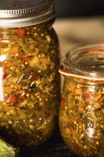 Homemade zucchini relish preserved in canning jars with fresh zucchini on the side.