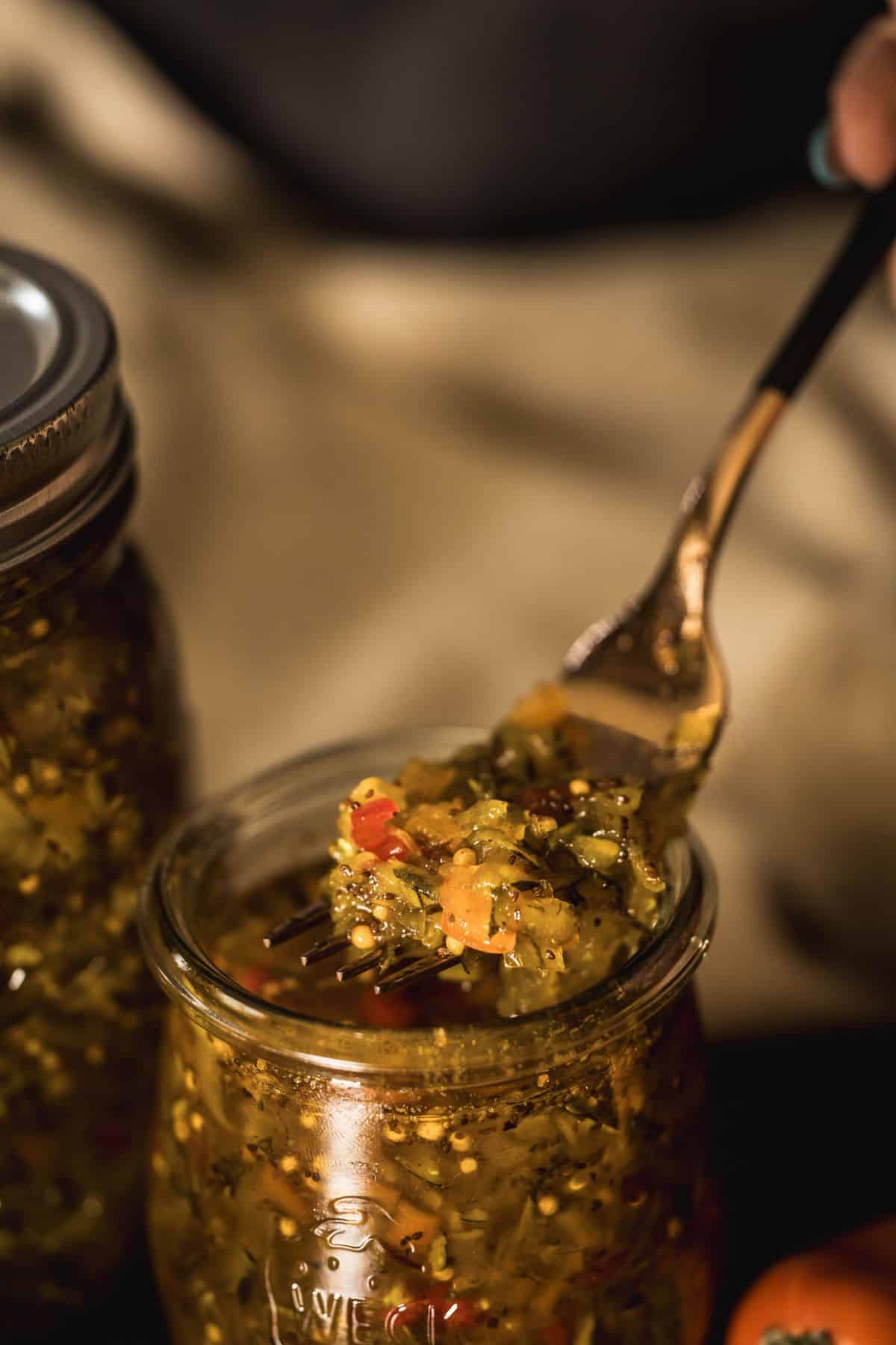 Fork lifting a bite of vibrant zucchini relish from a glass jar, showing texture and colorful ingredients.