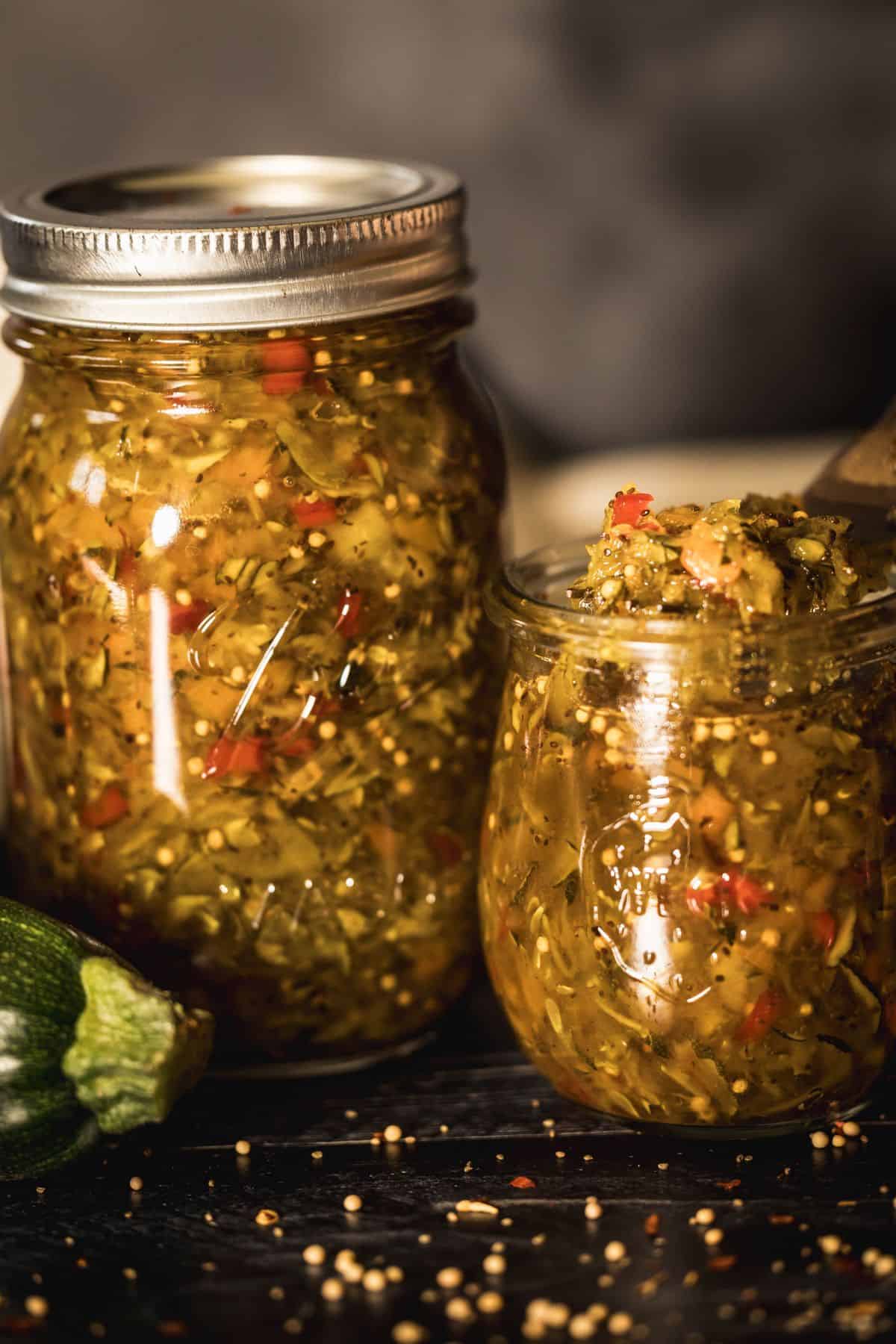 Close-up of zucchini relish in a glass jar with one jar partially open and relish scooped on a fork.